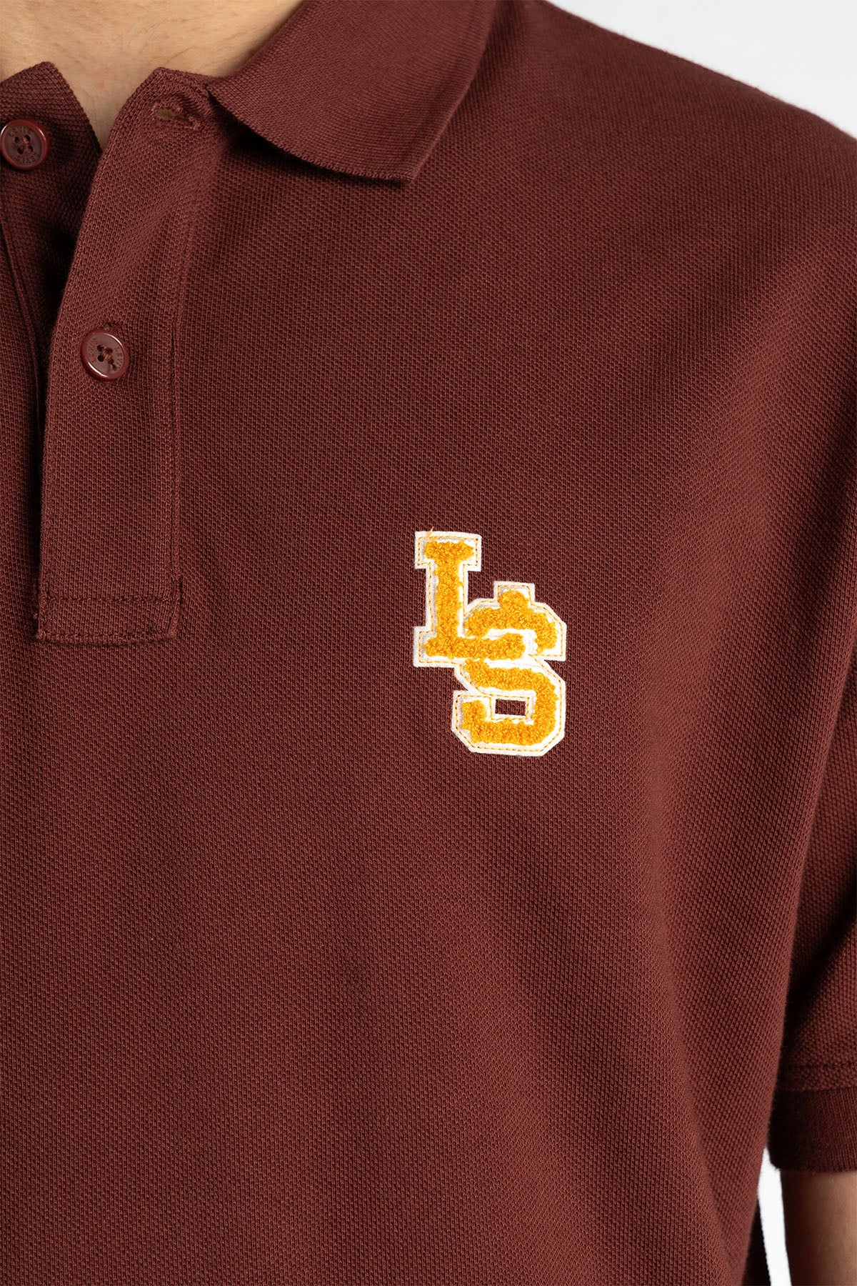 Maroon polo shirt fabric close-up with logo on chest and buttoned collar