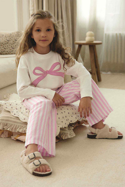 Girls' white bow top and pink striped pants, seated three-quarter view