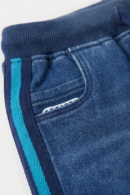 Blue jogger pants close-up: elastic waistband, drawstring, teal stripe trim, logo detail
