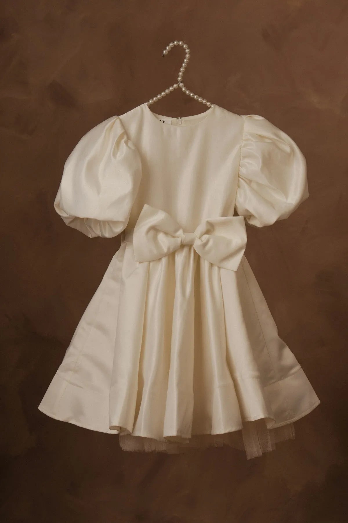White puff-sleeve dress with bow belt and layered tulle hem, on hanger