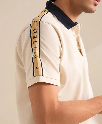 Off-white polo shirt sleeve with navy trim and vertical "FITTED" lettering.