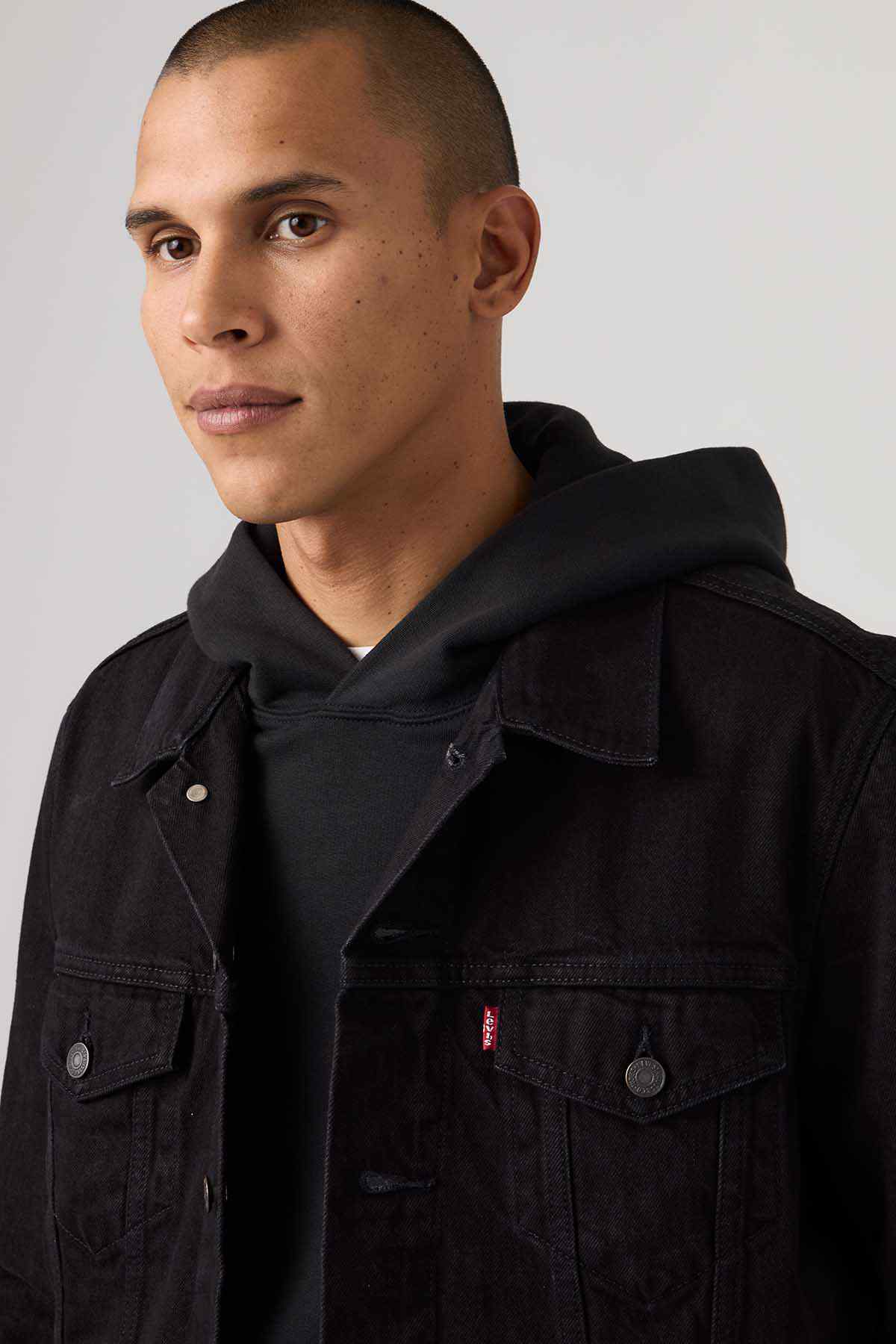 Black denim jacket with stand collar and flap chest pockets; hoodie underneath visible