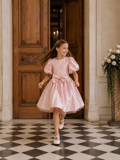 Pink satin-style dress with puff sleeves and bow at waist, knee-length.