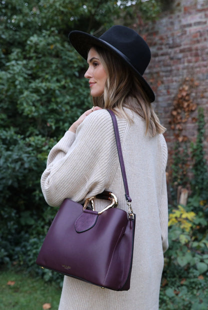 Purple handbag with top handle rings and crossbody strap, side view