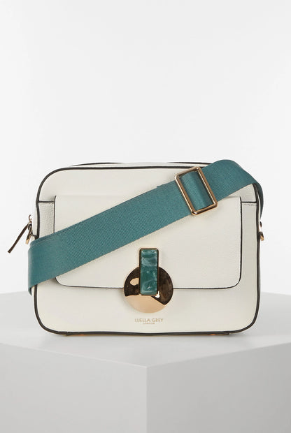 White flap crossbody handbag with teal webbing strap and gold trim, front logo detail
