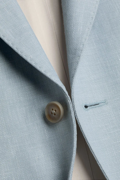 Light blue blazer fabric close-up with gold-toned button and pocket detail
