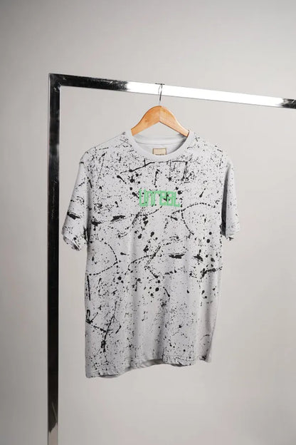 Light grey graphic T-shirt with black paint splatter and green logo on chest