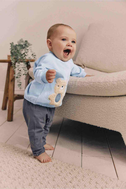 Light blue baby sweatshirt with teddy bear applique visible on the front