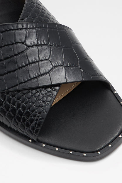 Black slide sandals close-up: embossed crocodile-texture upper and studded edge sole