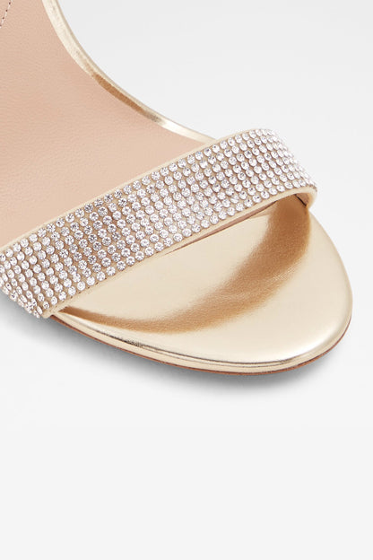Gold sandal close-up: rhinestone strap over open toe with stiletto heel.