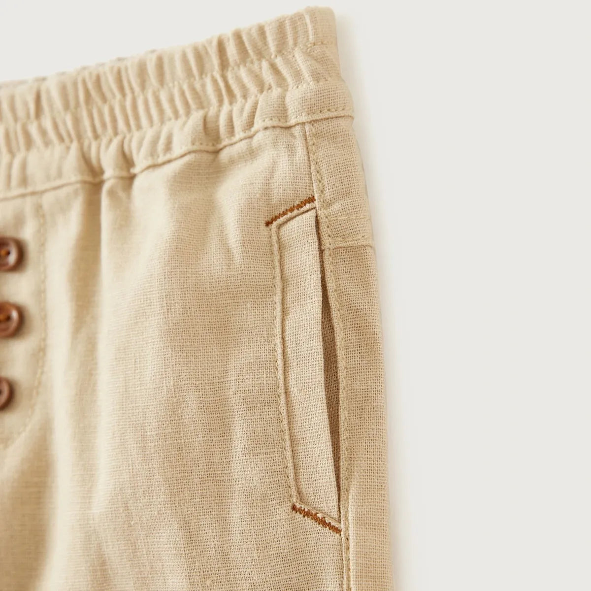 Beige baby trousers detail: elastic waistband and side seam pocket with contrast trim