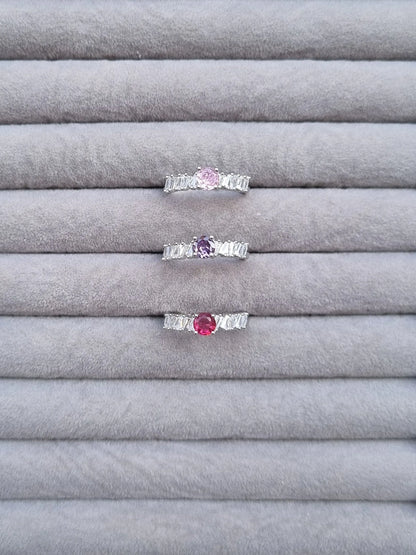 Three silver-tone rings with baguette stones and pink, purple, red center gemstones