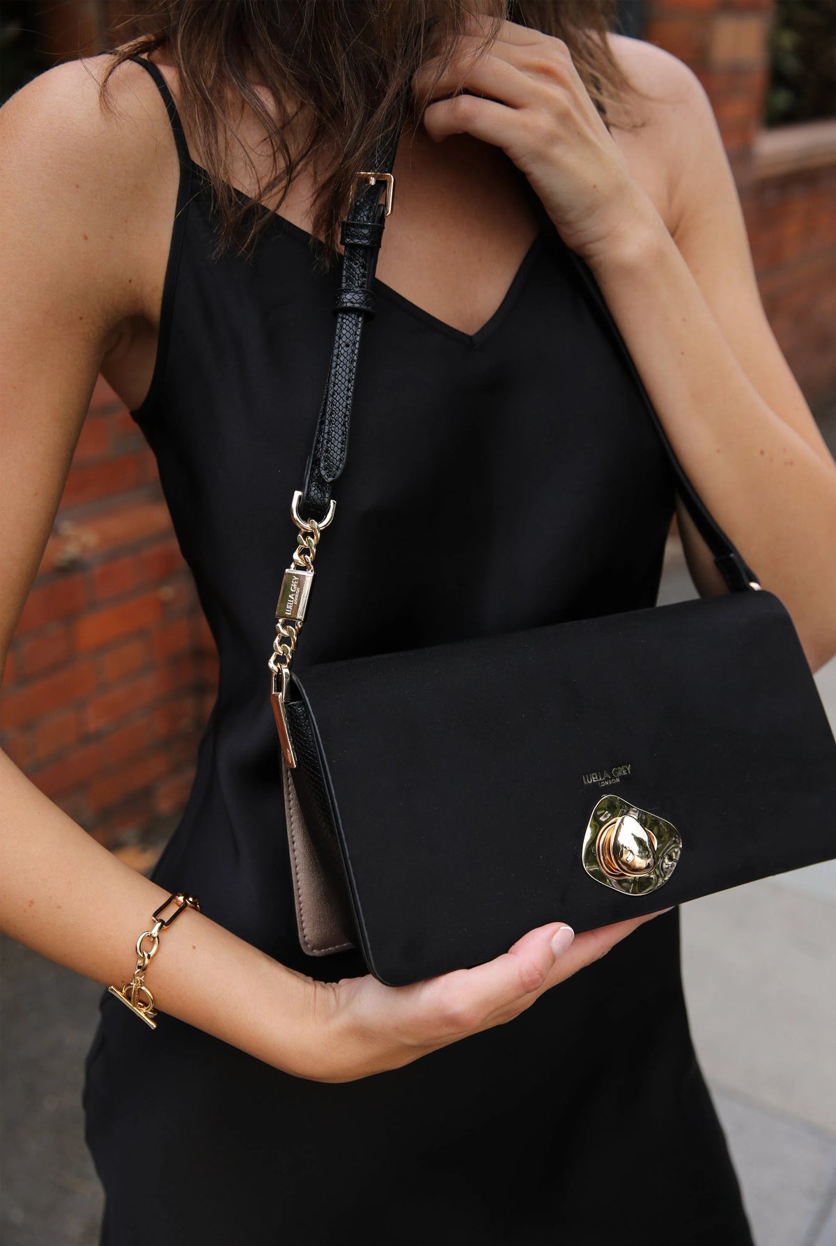 Black shoulder bag in hand with gold front emblem and chain shoulder strap