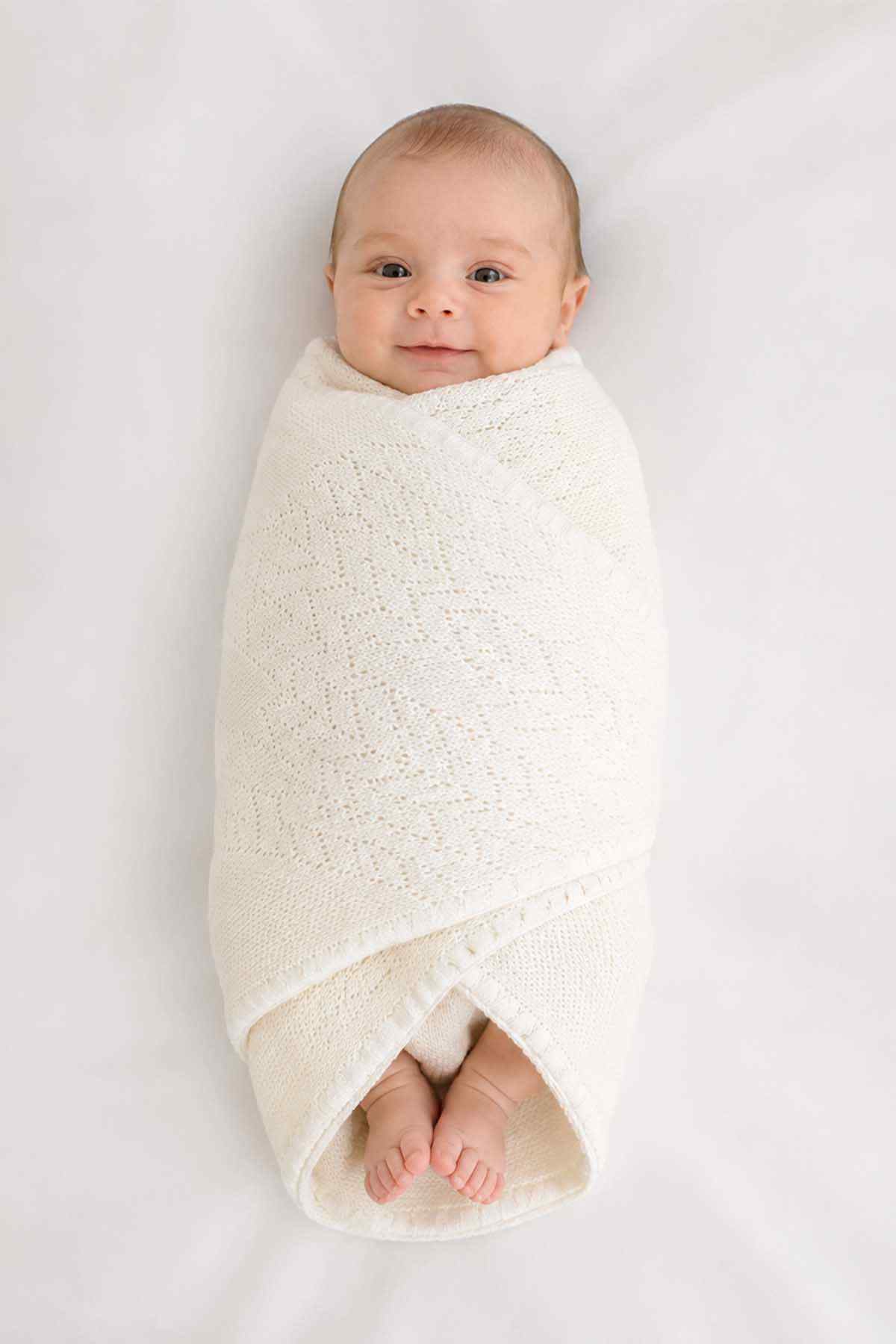 Baby shawl, white knitted wrap with open weave, tucked around a baby