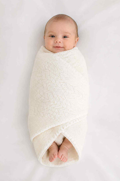 Baby shawl, white knitted wrap with open weave, tucked around a baby