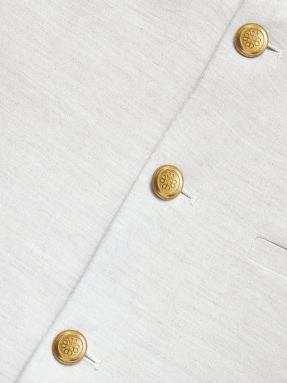 Beige waistcoat fabric close-up with gold logo buttons and stitched seams