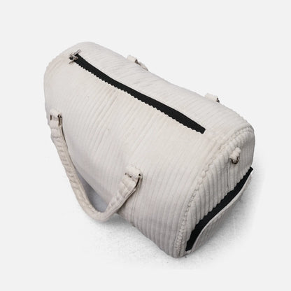 Cream duffel bag with black zipper pocket panel, padded handles, and metal rings
