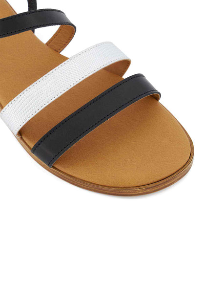 Black and white flat sandals with wide cross straps and tan sole