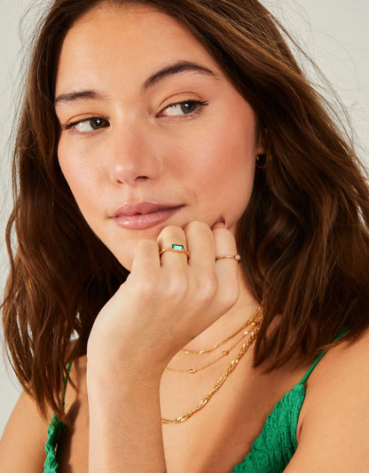 Gold-tone rings with green baguette gemstone and crystal details on hand