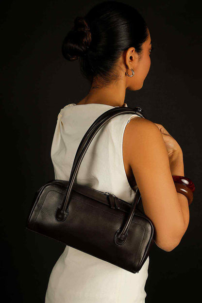 Dark-brown handbag viewed from back with top handles and shoulder-strap attachment.