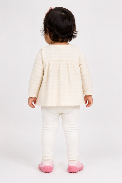 Baby outfit in back view: cream top with yoke detail, white leggings, pink socks