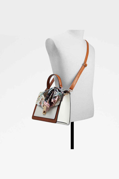 Handbag on mannequin with tan leather, patterned bow top, and shoulder strap