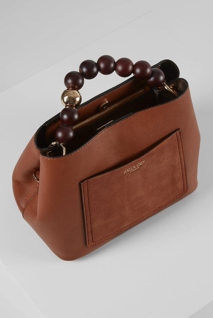 Brown leather handbag with beaded handle, top zipper, and front patch pocket.