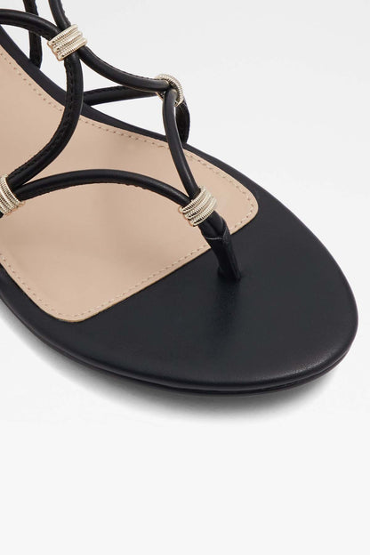 Black flat sandal toe strap detail with gold-tone ring accents