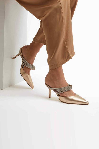 Gold heeled mule worn with woven ankle strap and pointed toe
