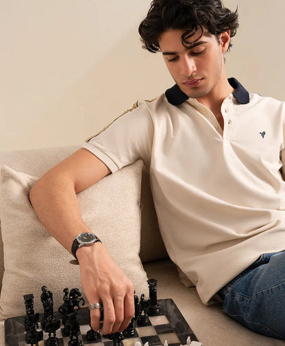 Fitted off-white polo shirt with navy collar and small chest logo; short sleeves.