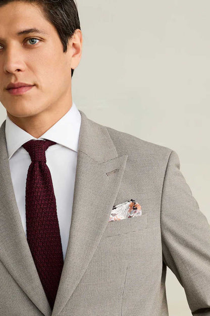 Men's light gray blazer lapel with burgundy tie and floral pocket square, close-up.
