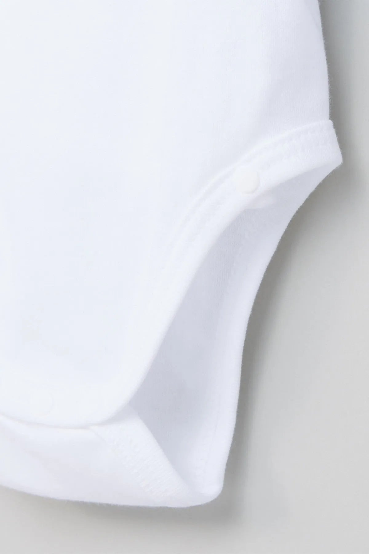 White baby bodysuit leg hem close-up with soft knit trim