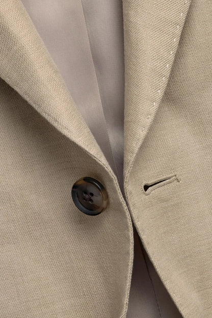 Men's beige suit jacket lapel with dark button and subtle textured fabric