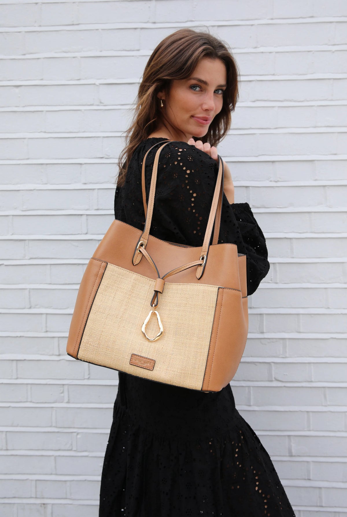 Tan woven tote bag with brown handles, center charm, and leather front patch