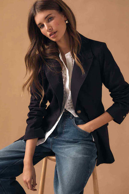 Navy blazer with white shirt and light blue jeans, model seated