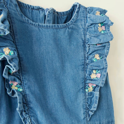 Blue denim romper close-up with floral-embroidered shoulder ruffles