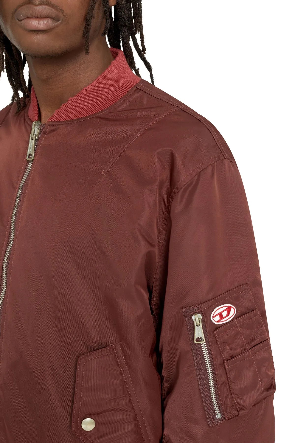 Brown bomber jacket close-up with zip pocket, snap button, and oval sleeve logo