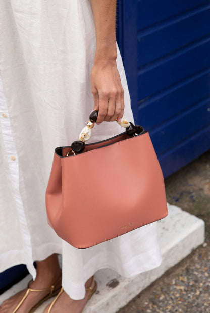 Pink handbag in hand with beaded top handles and structured silhouette