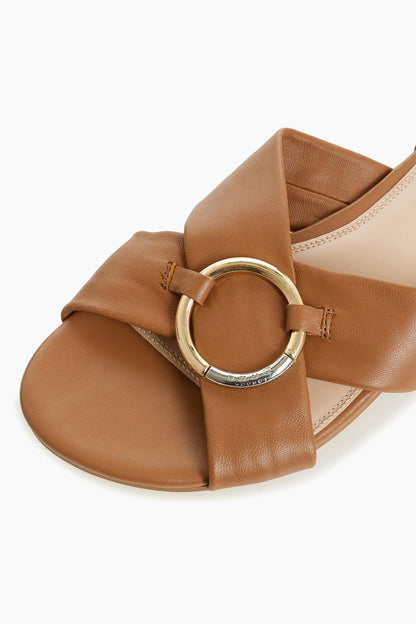 Tan leather sandal with large circular buckle on crossover strap and padded footbed