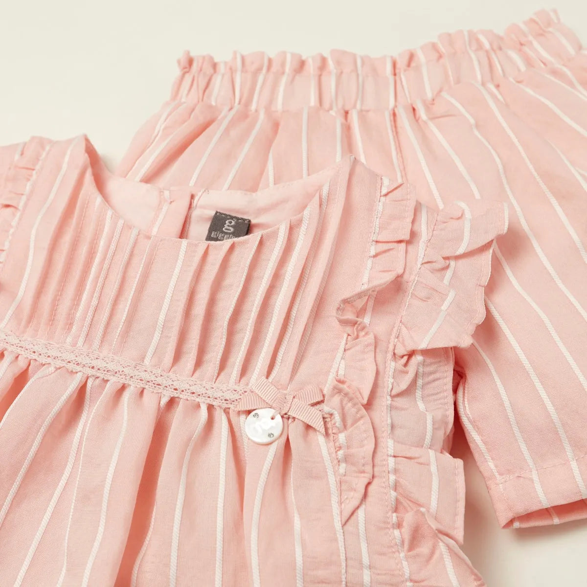 Close-up of pink striped baby dress bodice with ruffles and round button detail