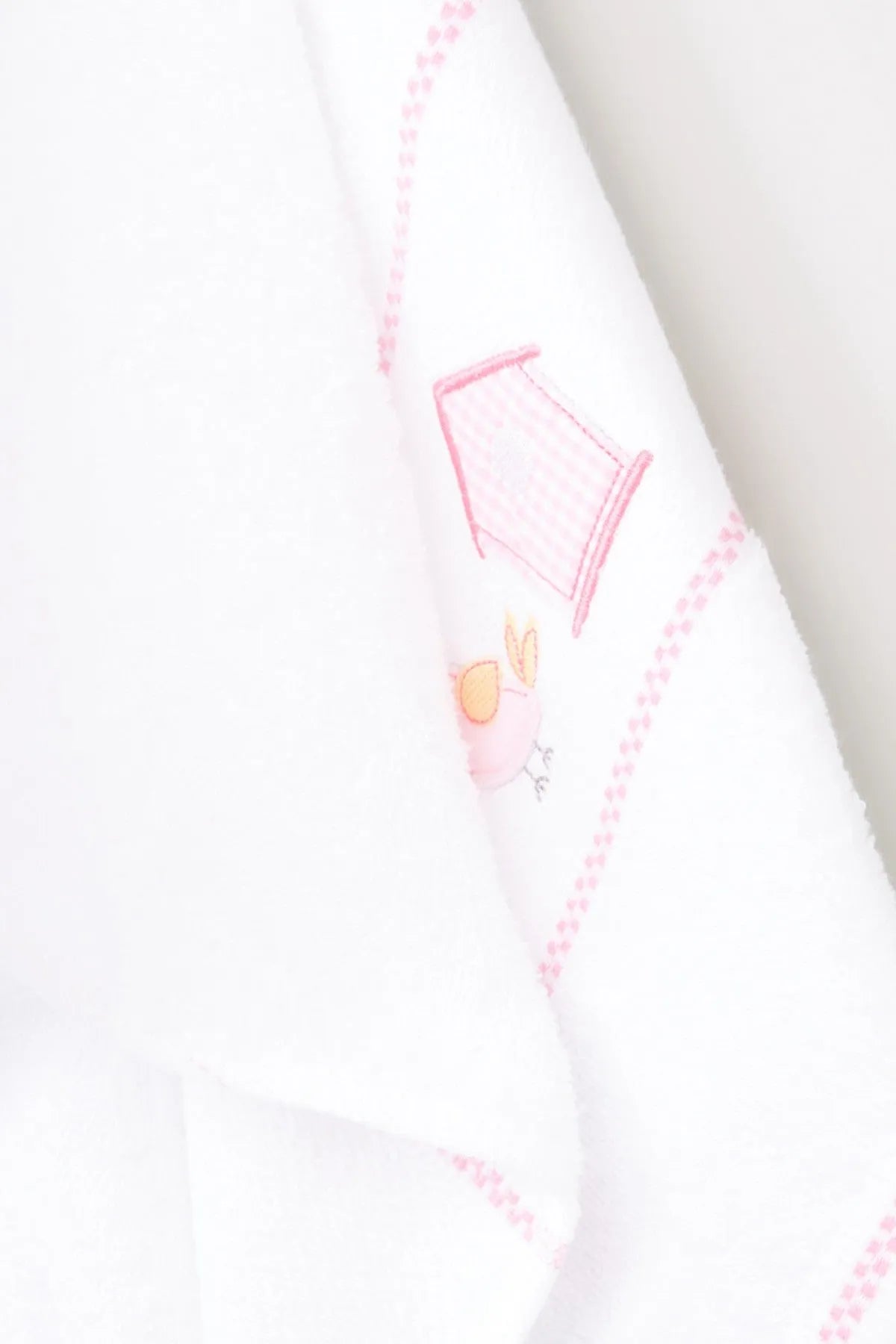 Corner close-up of white baby blanket with pink dotted border and bunny-house embroidery