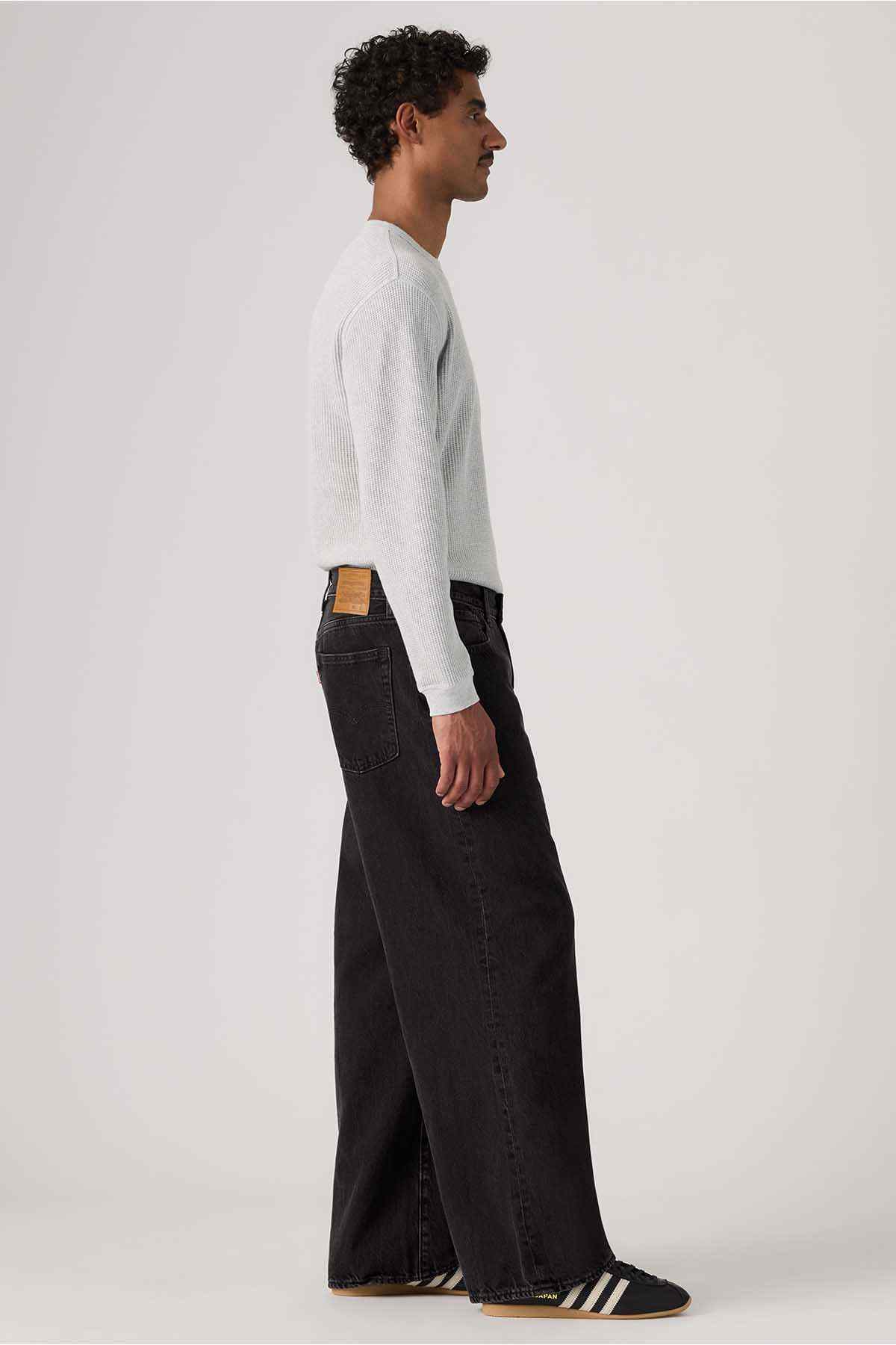 Black denim wide-leg jeans side view with leather logo patch on waistband