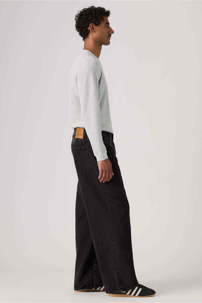 Black denim wide-leg jeans side view with leather logo patch on waistband