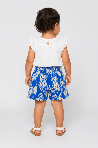 Back view toddler outfit: white top with eyelet shoulders and blue patterned shorts