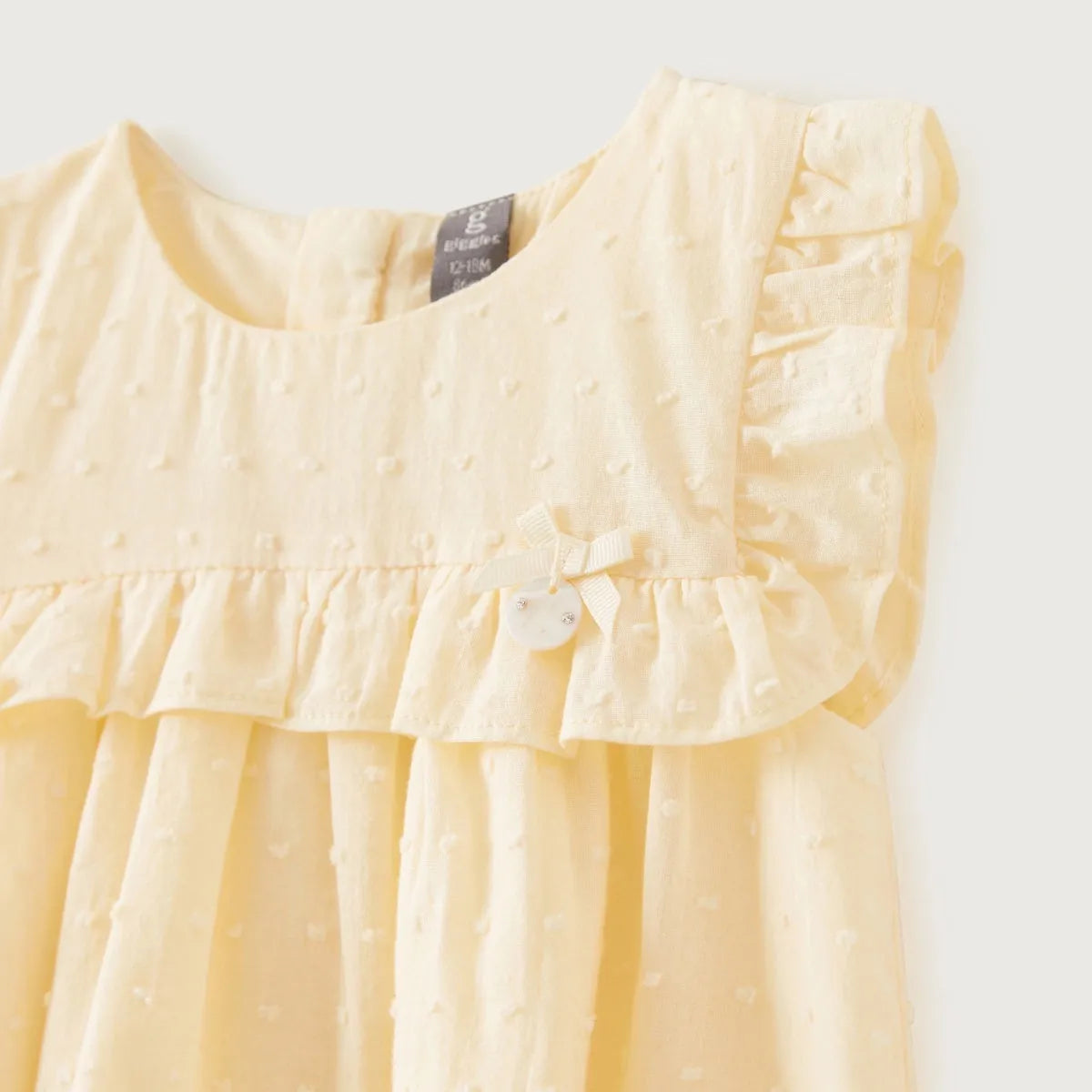 Baby dress close-up in light yellow with ruffle hem and waist bow detail