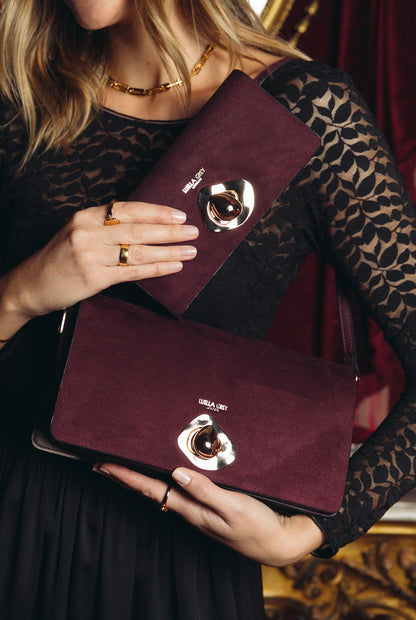 Purple flap bag held in hands with round gold clasp hardware