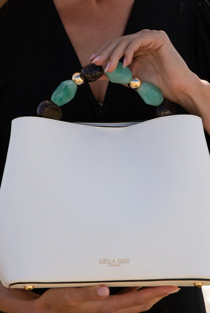 White handbag close-up with green-and-brown beaded handle and gold-tone clasp