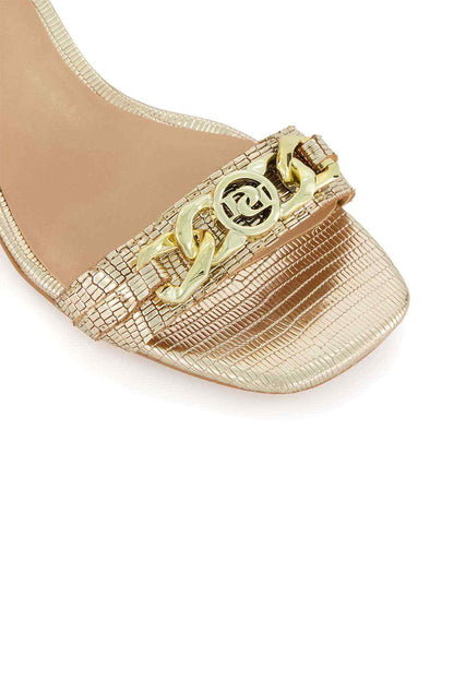 Gold sandal toe with textured straps and ornate logo buckle, open-toe design