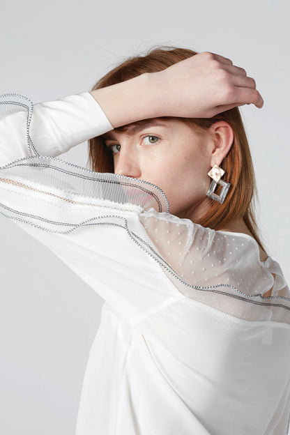 White sheer blouse close-up with ruffled neckline and chain-trim shoulder
