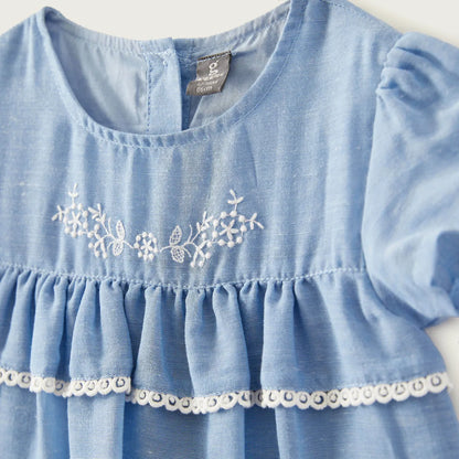 Blue baby dress close-up: gathered bodice, white lace trim, snowflake embroidery